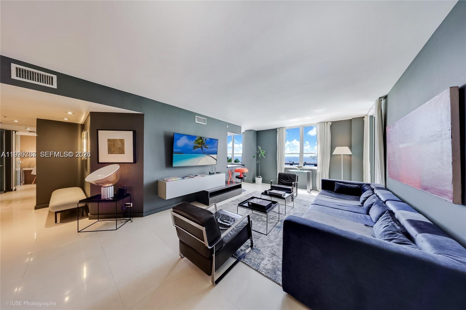 A modern living room features a blue sofa, leather armchairs, and a wall-mounted television — 701 Brickell Key Blvd # 503, Miami FL 33131, MIAMI, FL