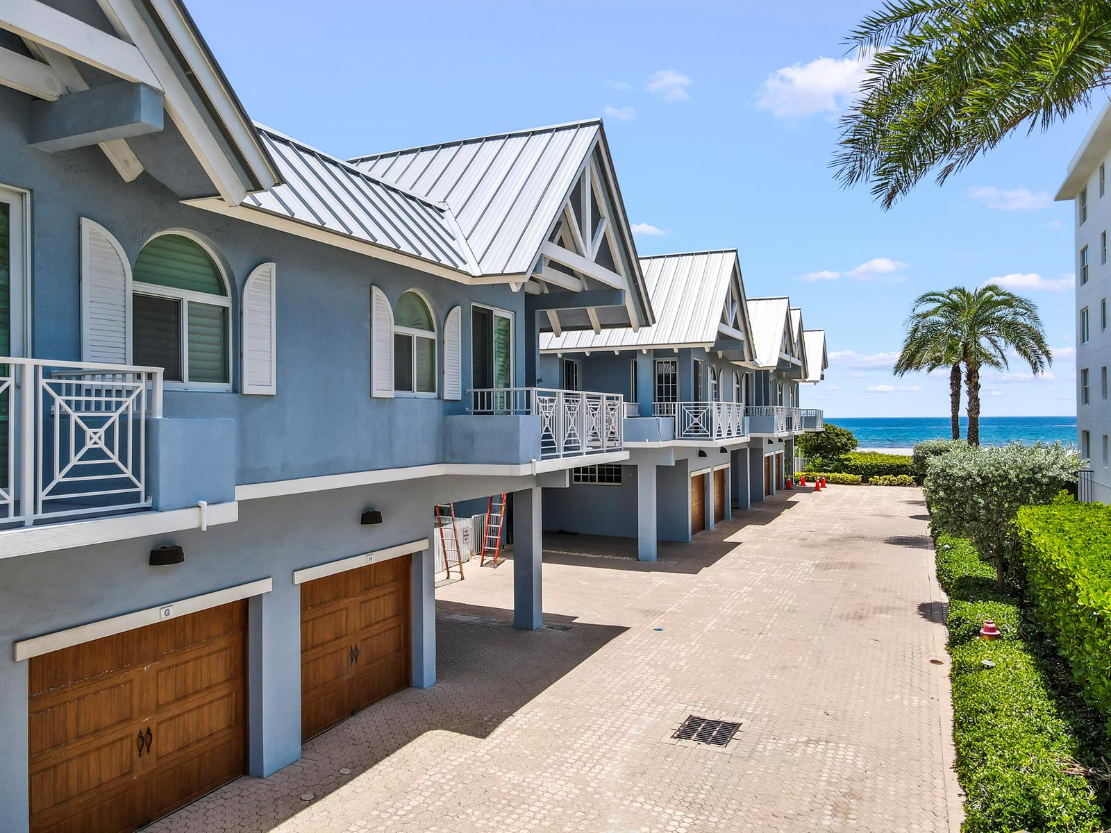 A row of blue multi-story townhomes with metal roofs and ground-level garages near the ocean — 1835 S Ocean Boulevard # H, Delray Beach FL 33483, DELRAY BEACH, FL