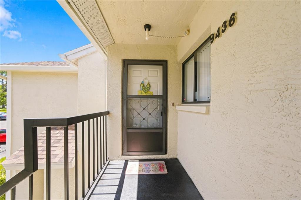 An exterior view of a covered entryway with a screen door and black metal railing — 9436 NAKOMA WAY UNIT 9436, WEEKI WACHEE, FL