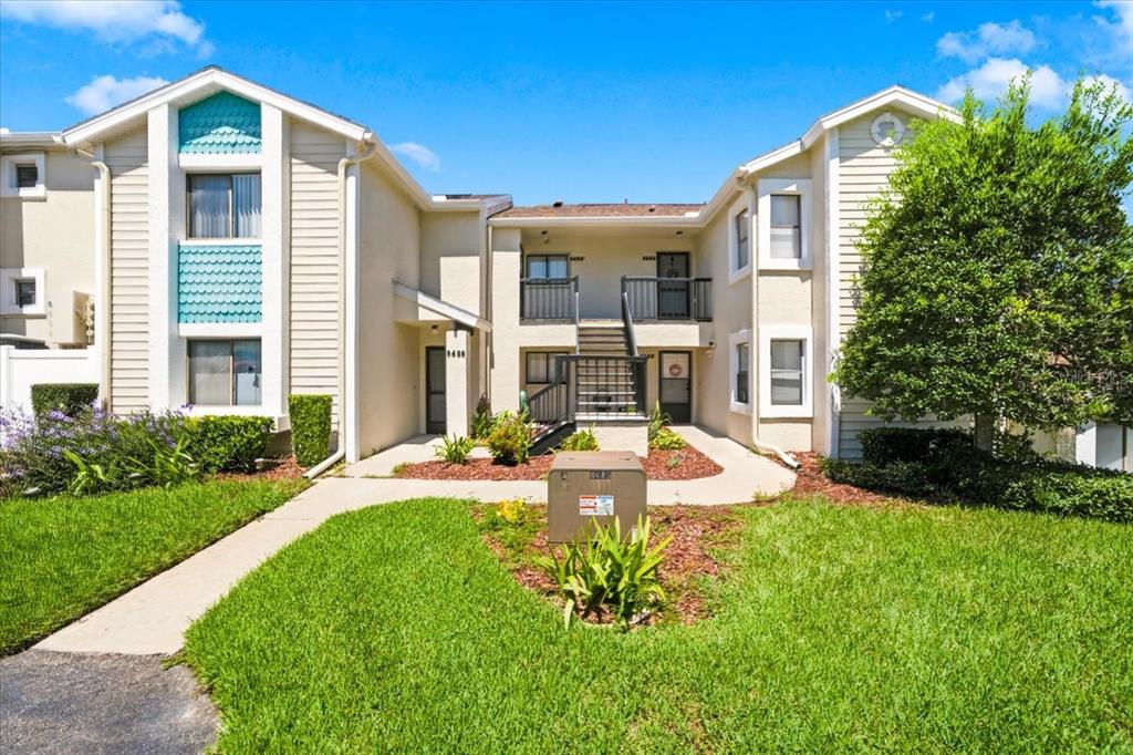 A two-story apartment building exterior features beige siding, a central staircase, and a grassy lawn — 9436 NAKOMA WAY UNIT 9436, WEEKI WACHEE, FL