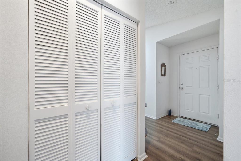 A hallway features white louvered closet doors, wood-look flooring, and a white front door — 9436 NAKOMA WAY UNIT 9436, WEEKI WACHEE, FL