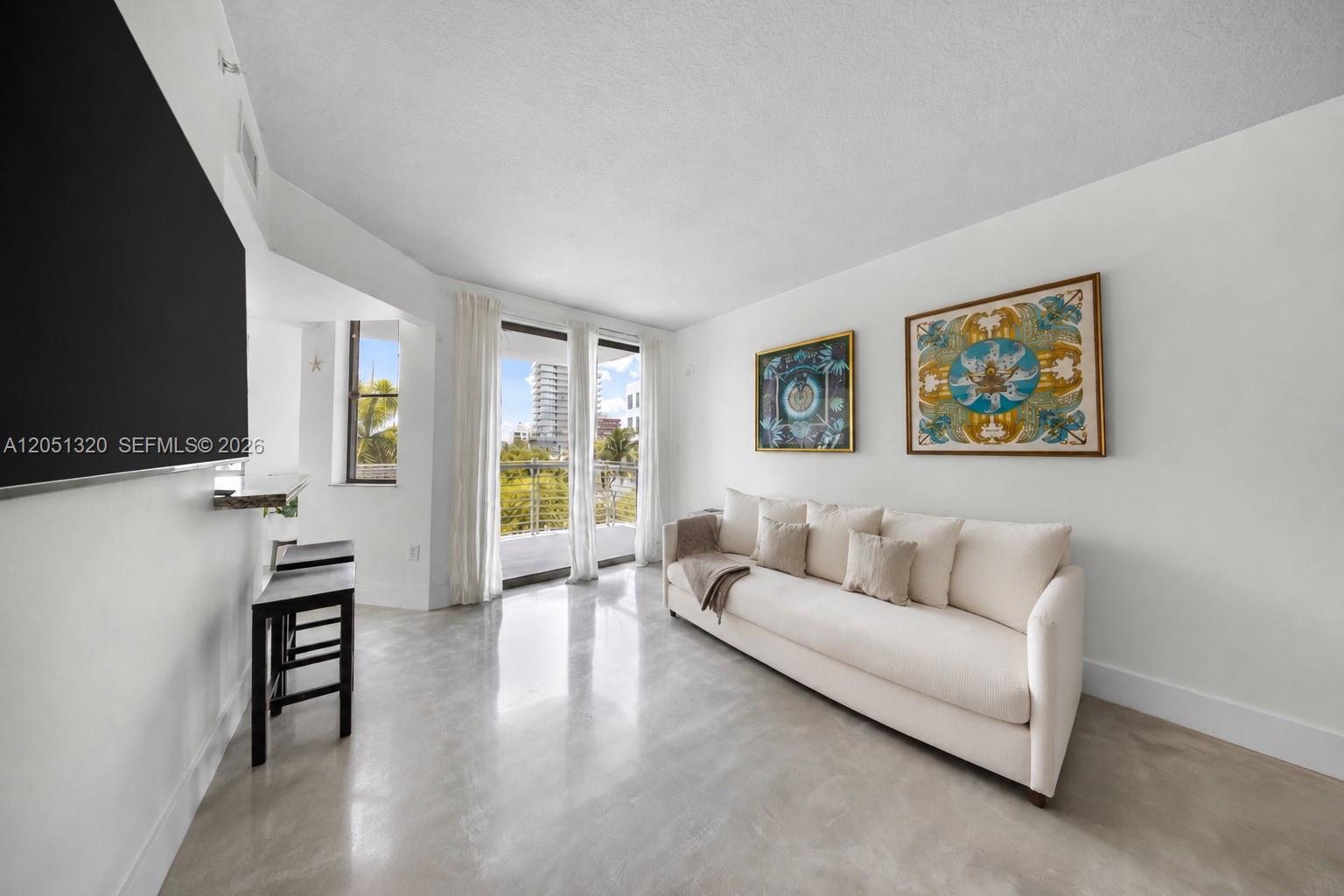 A living room features a white sofa, concrete floors, and a balcony with city views — 110 Washington Ave # 2505, Miami Beach FL 33139, MIAMI BEACH, FL