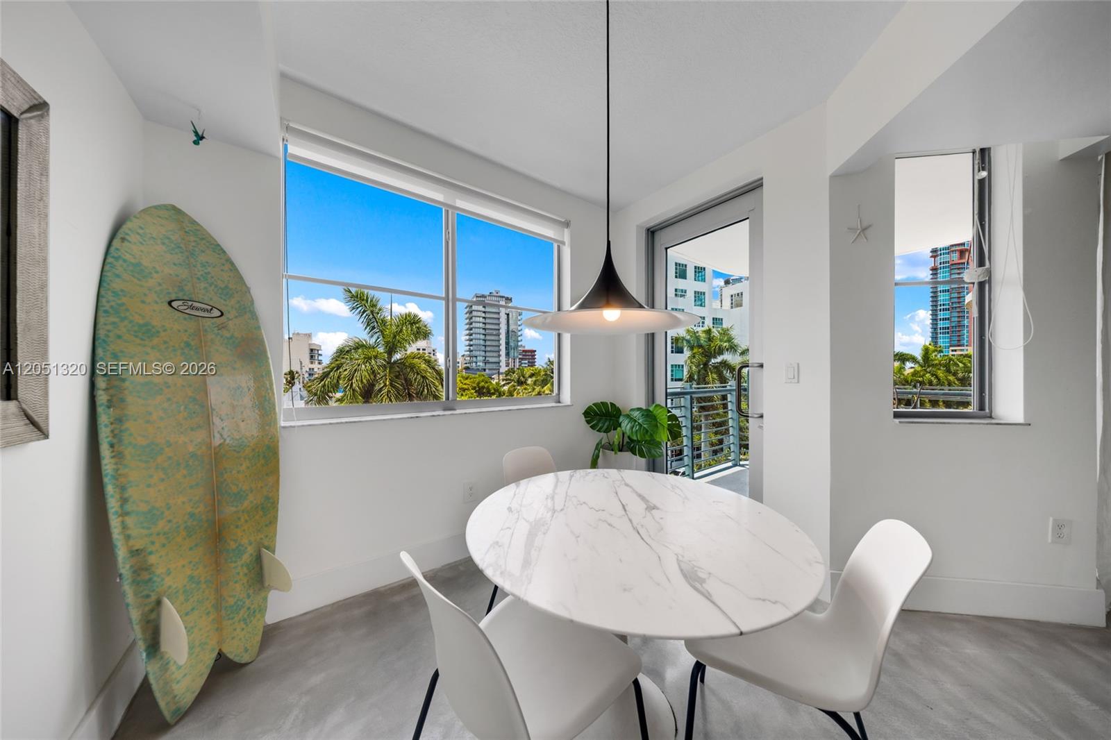 A dining area features a marble table, white chairs, a surfboard, and city views — 110 Washington Ave # 2505, Miami Beach FL 33139, MIAMI BEACH, FL