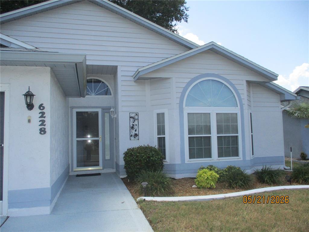 A light blue house exterior features a front entrance, a large arched window, and landscaping — 6228 EGRET DRIVE, LAKELAND, FL