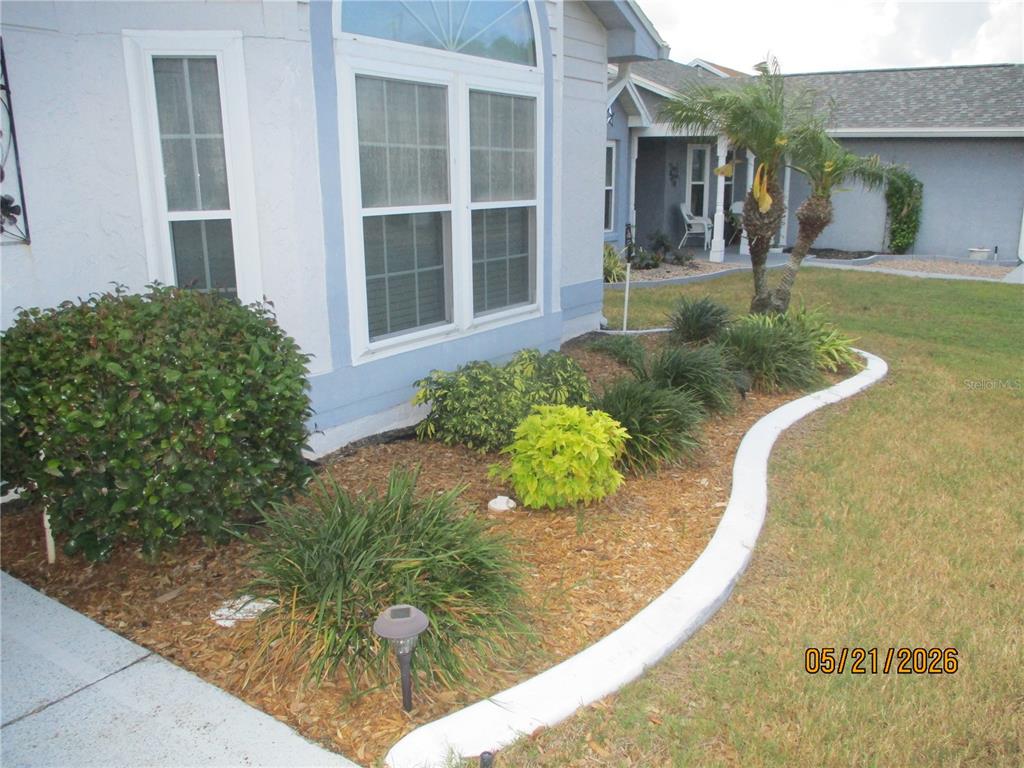 A landscaped garden bed with mulch and shrubs sits in front of a light blue house — 6228 EGRET DRIVE, LAKELAND, FL