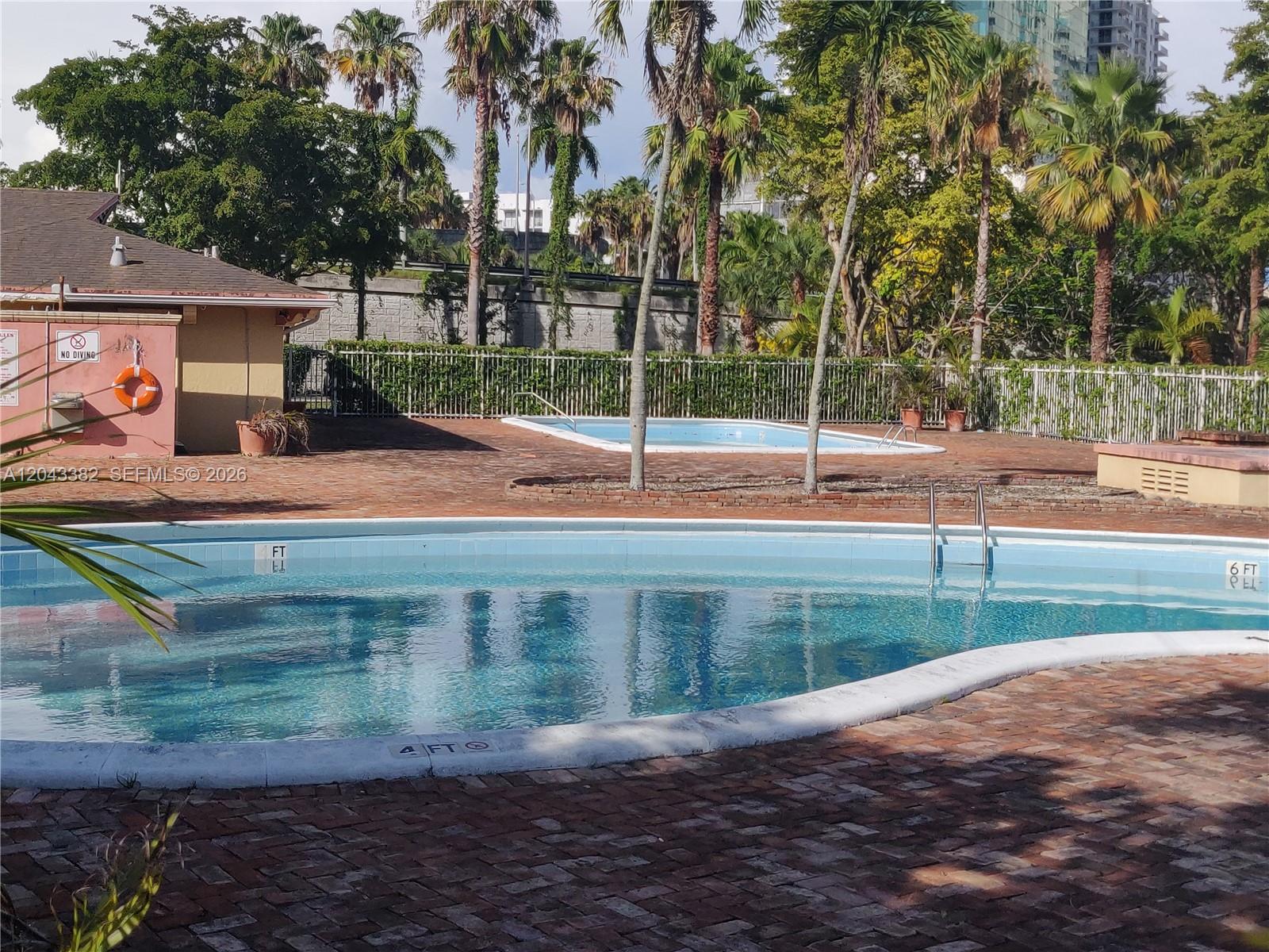 An outdoor pool area features two swimming pools surrounded by brick pavers and palm trees — 9001 SW 77th Ave # C606, Miami FL 33156, MIAMI, FL