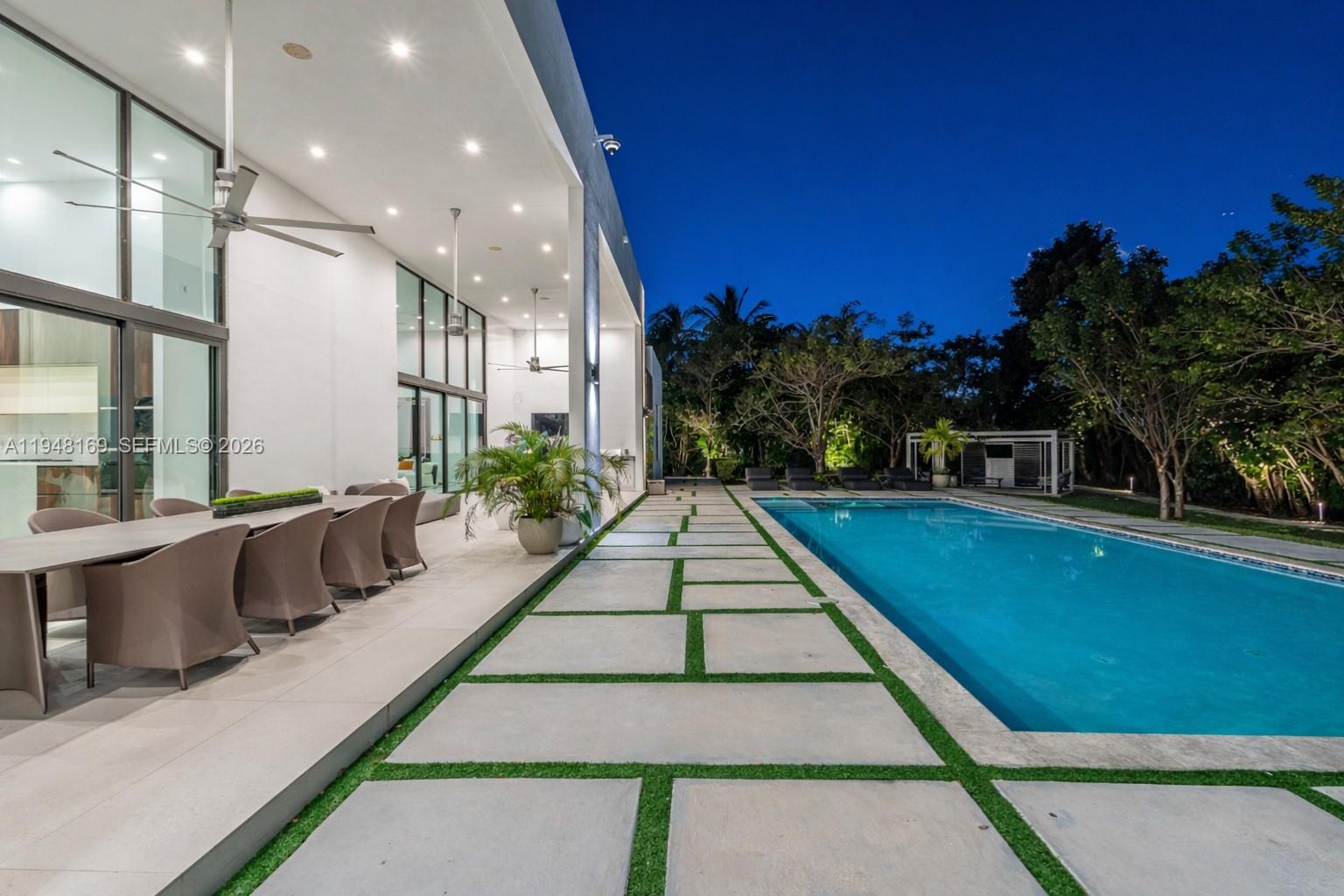 A modern patio features a dining set, a long swimming pool, and stone pavers — 6175 SW 128th Street, Pinecrest FL 33156, PINECREST, FL