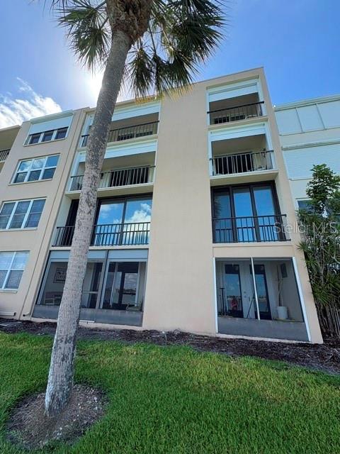 A low-angle view of a multi-story tan apartment building with balconies and a palm tree — 7920 SUN ISLAND DRIVE S UNIT 205, SOUTH PASADENA, FL