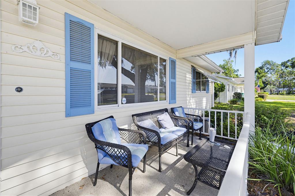 A covered front porch features light-colored siding, blue shutters, and black wicker patio furniture — 10952 SW 75TH AVENUE, OCALA, FL