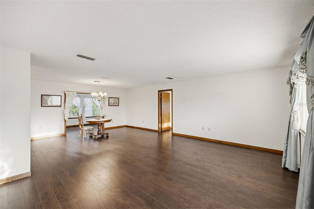 A spacious, empty room with dark wood flooring, white walls, and a small dining area — 10952 SW 75TH AVENUE, OCALA, FL