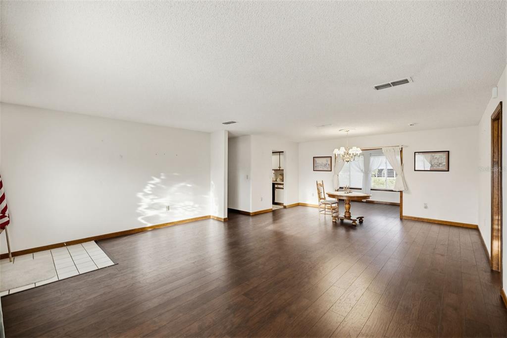 A spacious room with dark wood flooring, white walls, and a small dining area — 10952 SW 75TH AVENUE, OCALA, FL