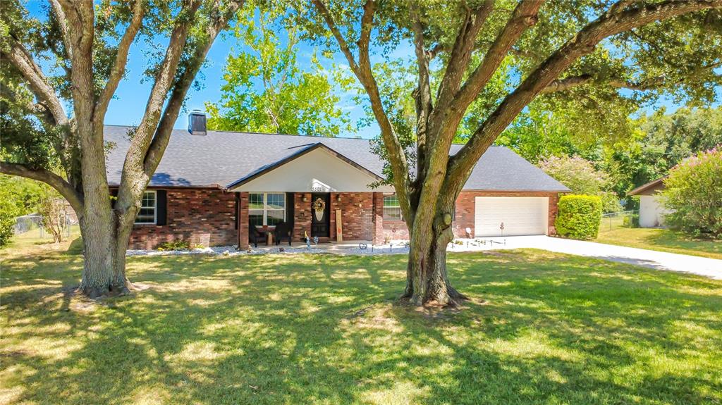 A single-story brick house with a dark roof, a two-car garage, and large shade trees — 5501 SE 42ND COURT, OCALA, FL