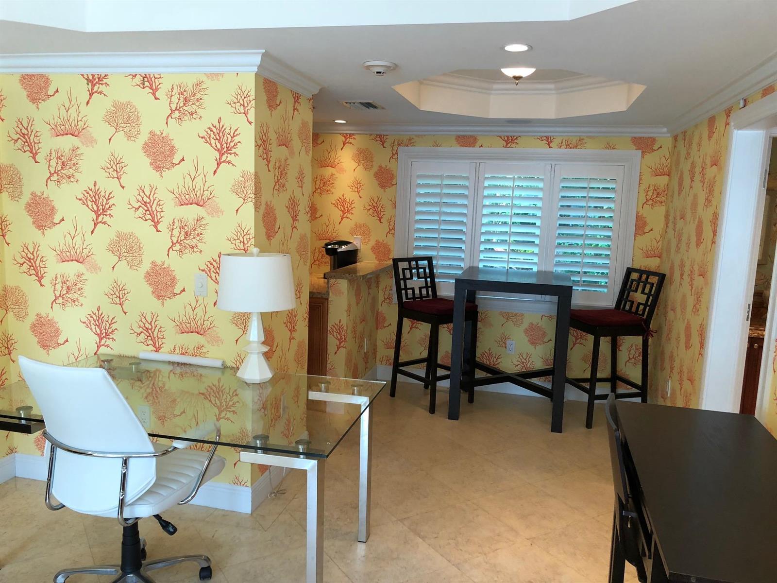 A home office featuring yellow coral-patterned wallpaper, a glass desk, and a small dining area — 251 Oleander Avenue # 1, Palm Beach FL 33480, PALM BEACH, FL