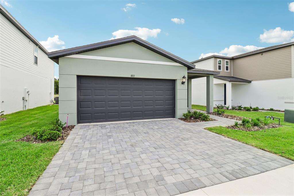 A light green house with a dark garage door and a paver driveway — 803 SUNSHOWER DRIVE, LADY LAKE, FL