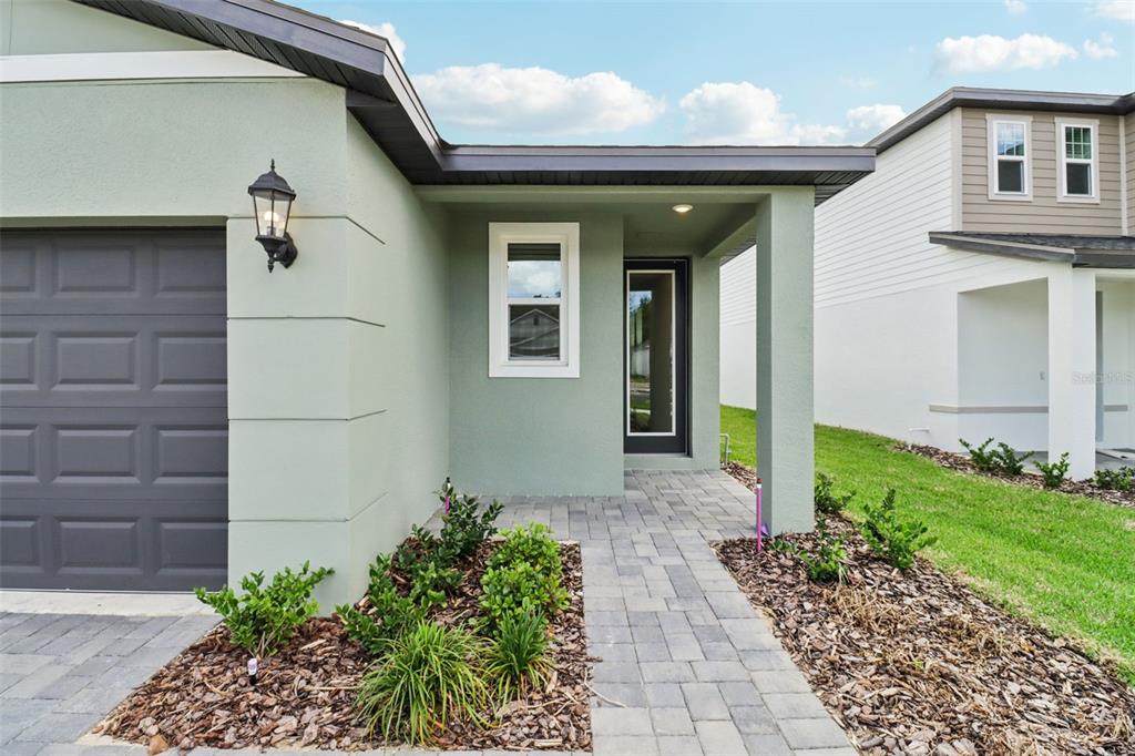 A light green house exterior features a gray garage door, a paved walkway, and landscaping — 803 SUNSHOWER DRIVE, LADY LAKE, FL