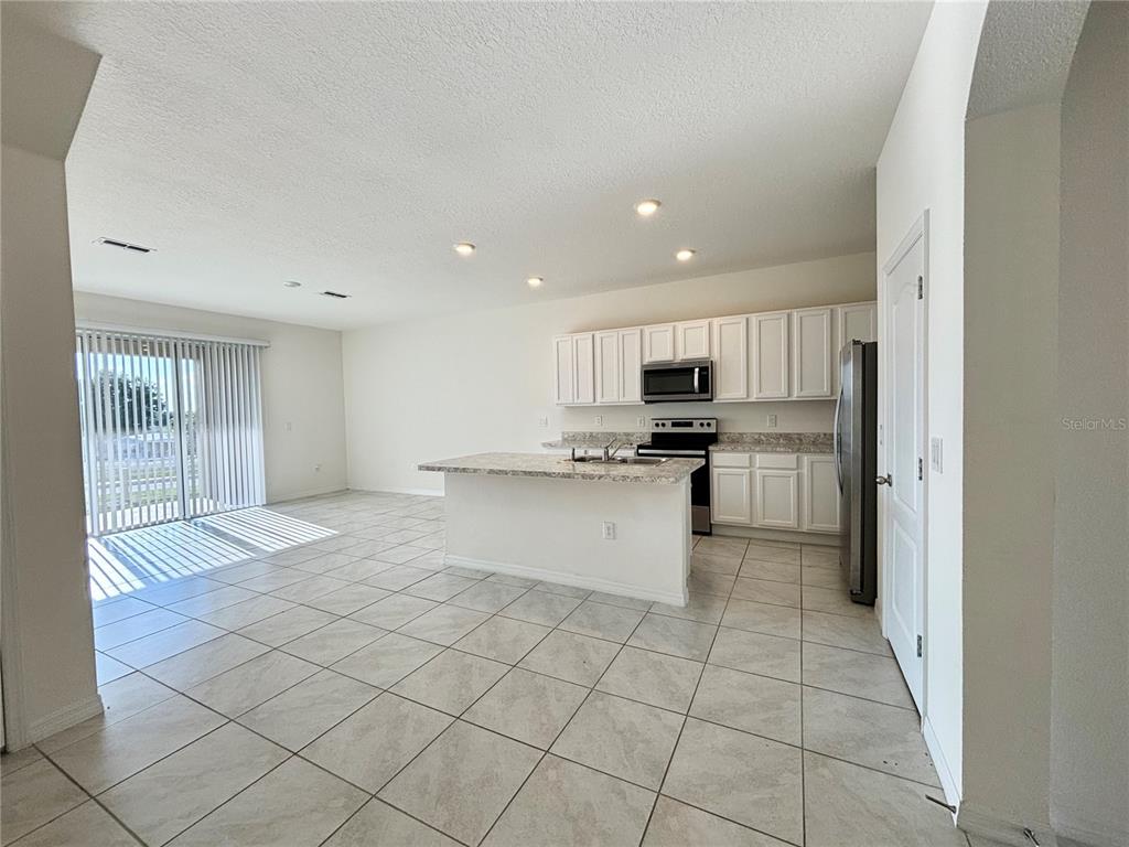 An open-concept kitchen and living area features white cabinets, granite countertops, and tile flooring — 401 FELTRIM RESERVE BOULEVARD, DAVENPORT, FL