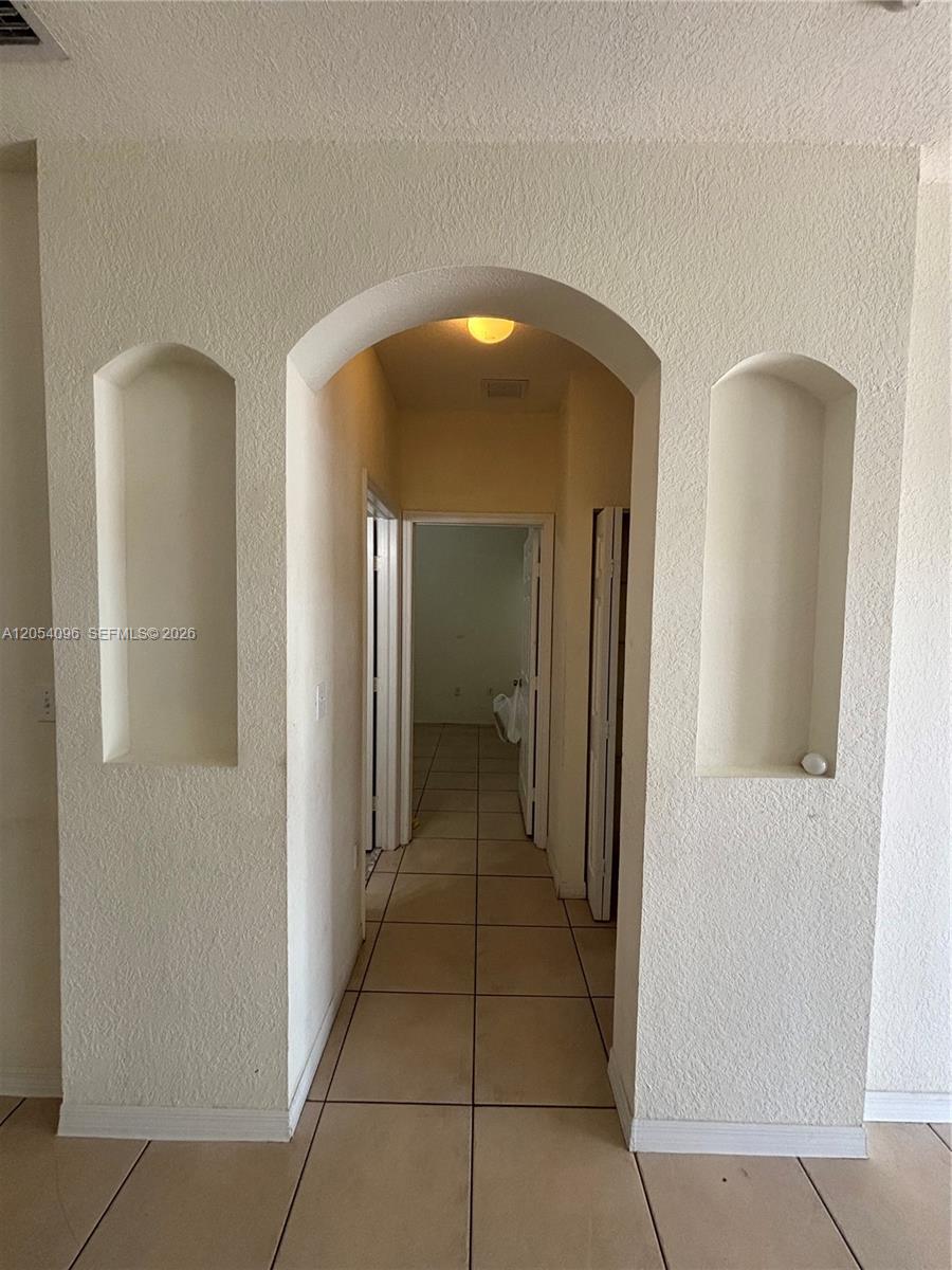 An arched hallway features two recessed wall niches and light-colored tile flooring — 13781 SW 171st Ter, Miami FL 33177, MIAMI, FL