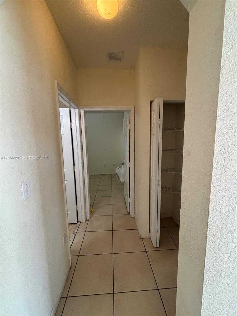A hallway with beige tile flooring leads to a doorway and an open closet — 13781 SW 171st Ter, Miami FL 33177, MIAMI, FL