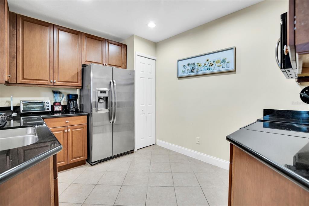 A kitchen features wood cabinets, black countertops, stainless steel appliances, and light-colored tile flooring — 7501 MOURNING DOVE CIRCLE UNIT 103, REUNION, FL