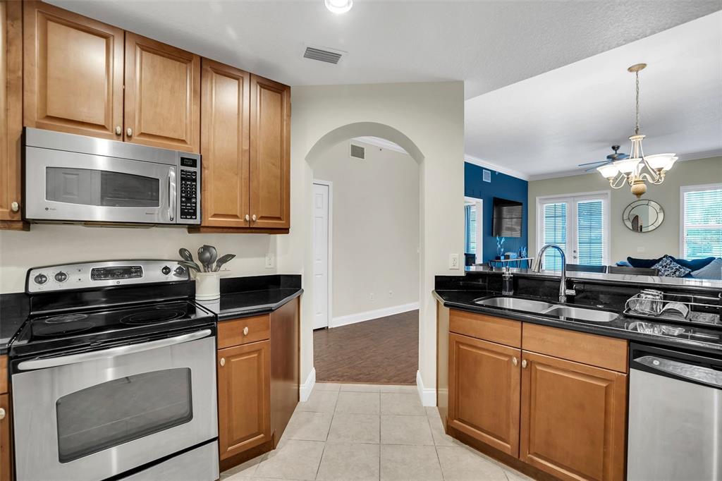 A kitchen features wood cabinets, black countertops, stainless steel appliances, and an arched entryway — 7501 MOURNING DOVE CIRCLE UNIT 103, REUNION, FL