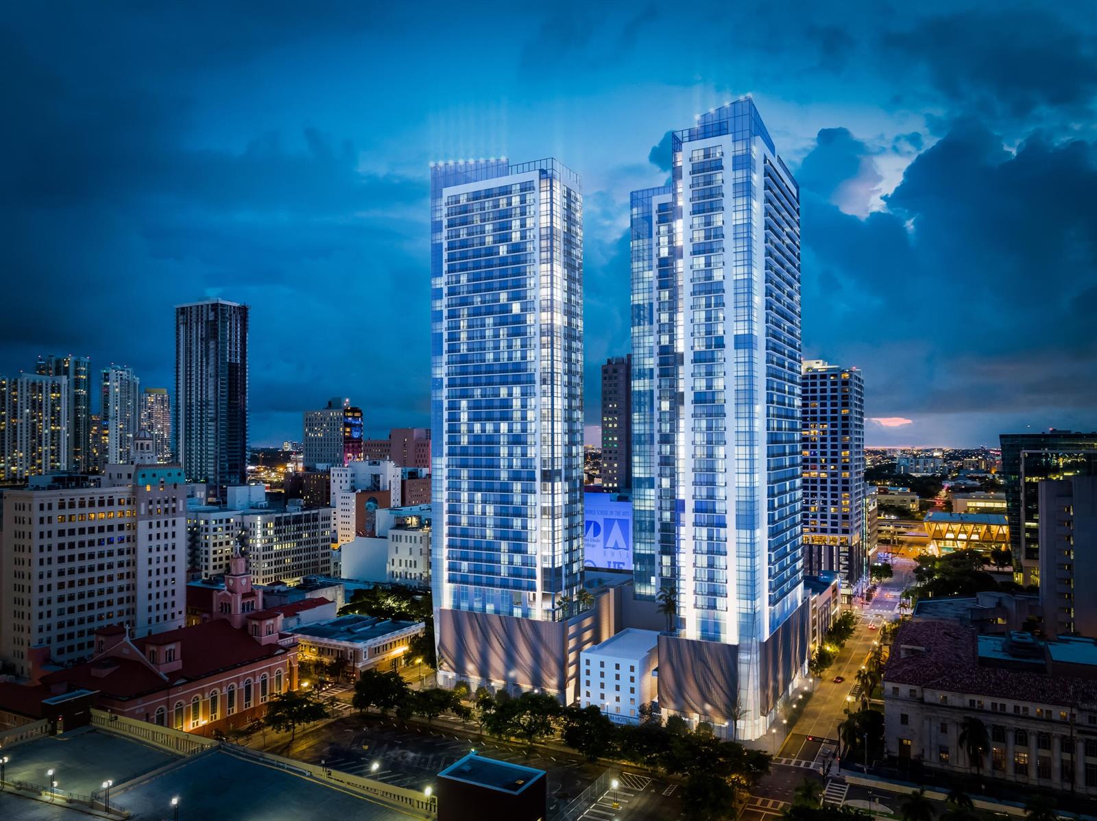 This architectural rendering shows two illuminated modern skyscrapers rising above a dense city at dusk — 55 NE 2nd Street # 2407, Miami FL 33132, MIAMI, FL