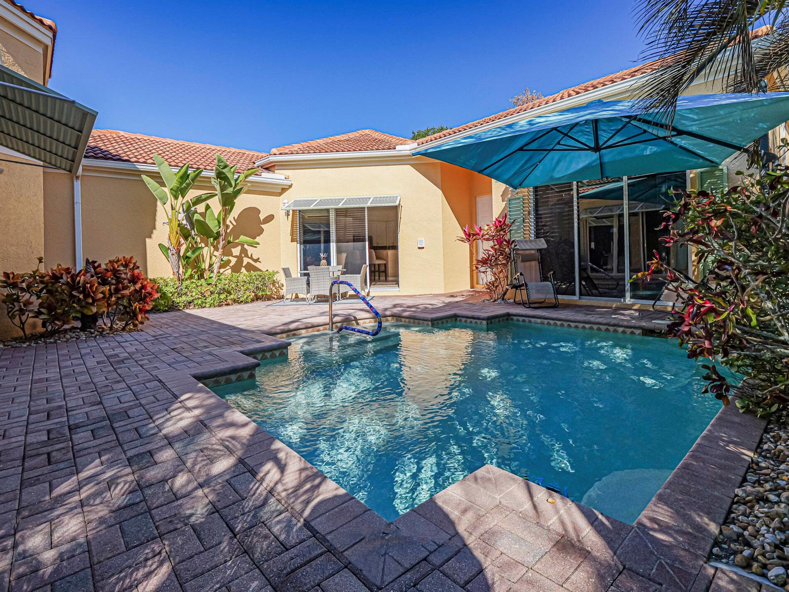 A backyard swimming pool with a blue umbrella and patio pavers next to a house — 9630 E Maiden Court, Vero Beach FL 32963, VERO BEACH, FL