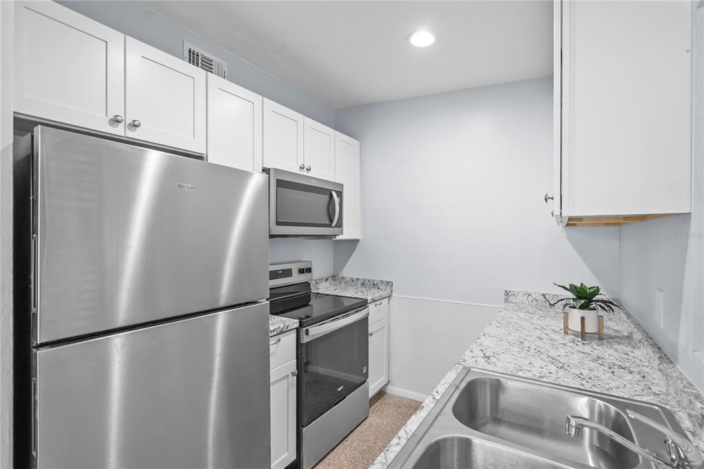 A kitchen features white cabinets, stainless steel appliances, and speckled granite countertops — 5212 N INDIANA AVENUE, WINTER PARK, FL