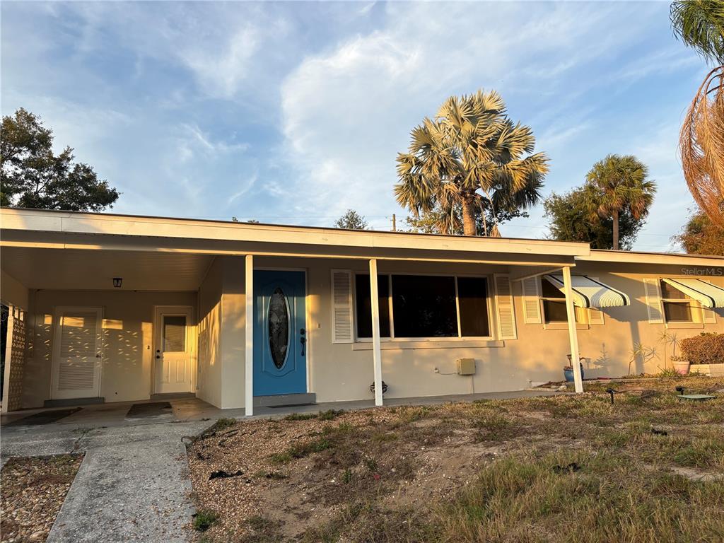 A single-story house features a blue front door, a carport, and a large palm tree — 719 HILLSIDE AVENUE, LAKE WALES, FL