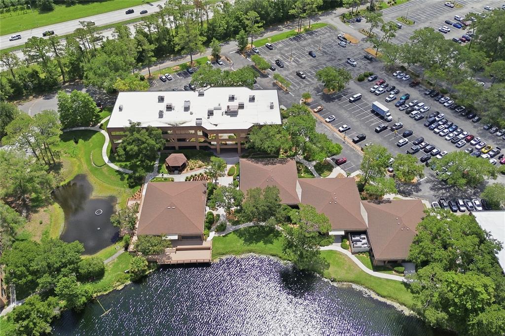 An aerial view shows a multi-story office building with a large parking lot and pond — 8669 BAYPINE ROAD, JACKSONVILLE, FL