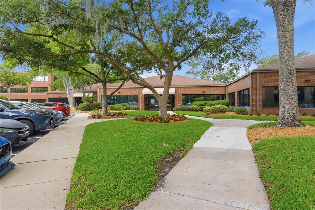 A brick office building with a parking lot, sidewalks, and large trees in the foreground — 8669 BAYPINE ROAD, JACKSONVILLE, FL