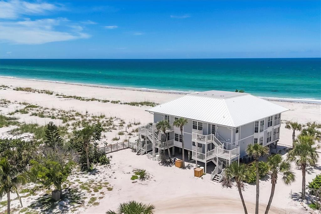 An elevated house with a white metal roof stands on a sandy beach by the ocean — 7554 PALM ISLAND DRIVE S UNIT 1813, PLACIDA, FL
