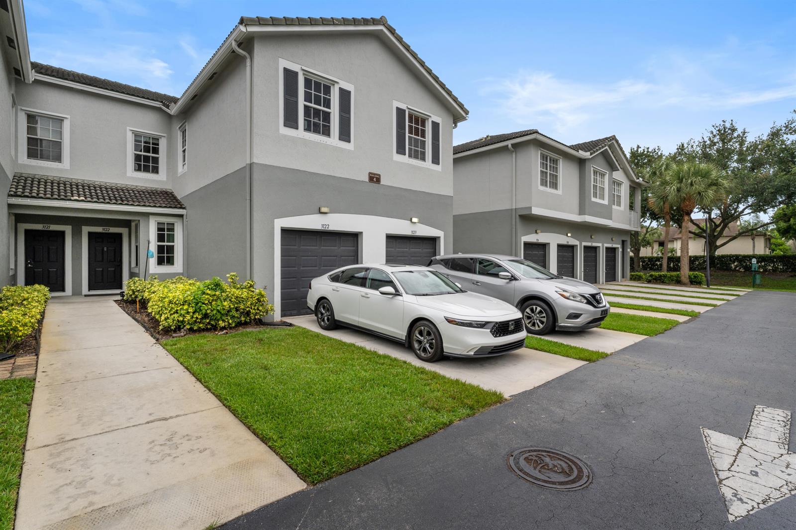A two-story residential building with gray stucco walls, dark garage doors, and two parked cars — 3122 Grandiflora Drive, FL 33467, FL