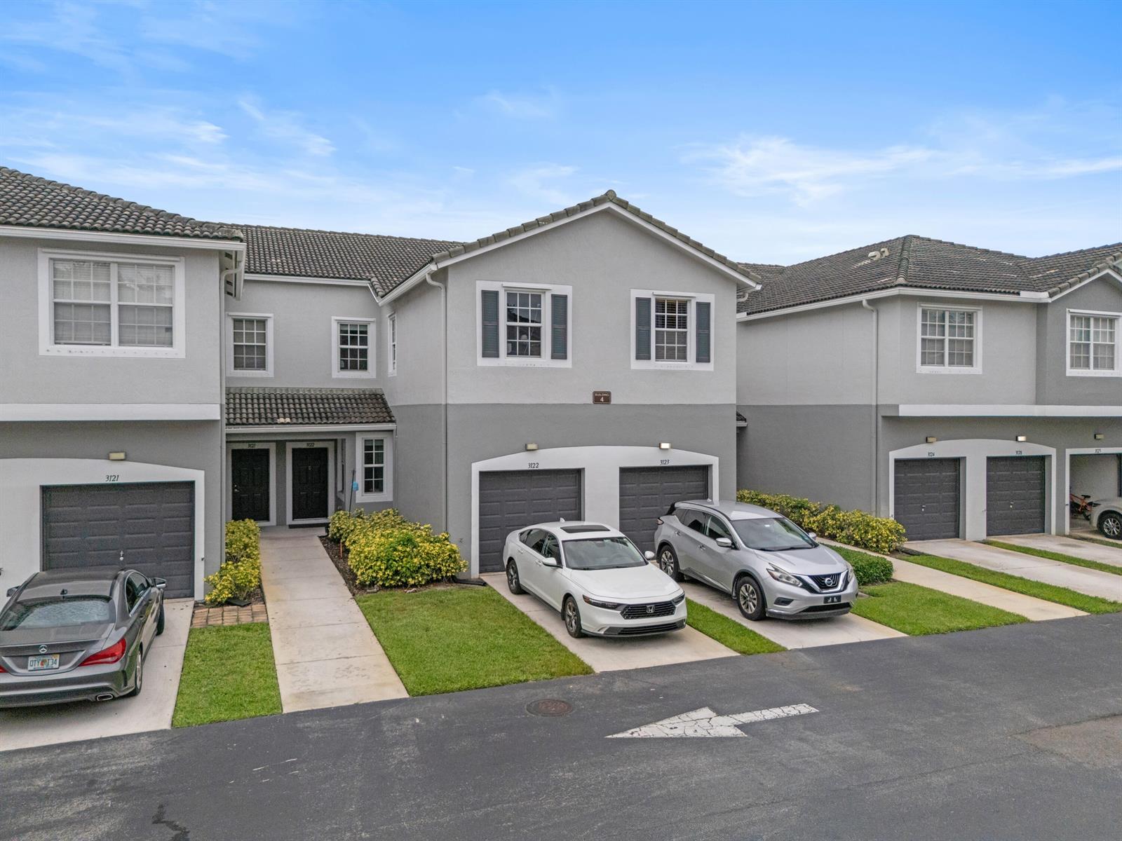 An exterior view of a multi-unit residential building with gray stucco walls and attached garages — 3122 Grandiflora Drive, FL 33467, FL