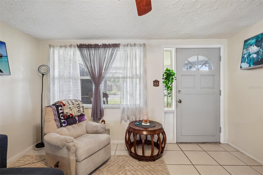 A living room features a beige recliner, a round wooden table, and a gray front door — 2049 MAUREEN DRIVE, HOLIDAY, FL