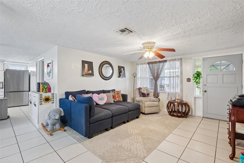 A living room features a blue sectional sofa, a beige armchair, and white tile flooring — 2049 MAUREEN DRIVE, HOLIDAY, FL