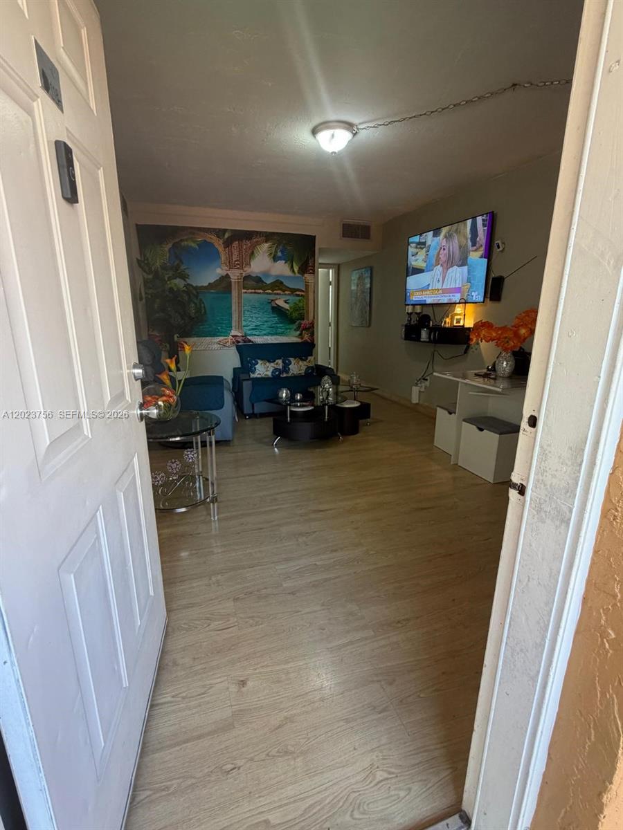 A living room features light wood-look flooring, a wall mural, and a wall-mounted television — 1245 W 24th St # 118, Hialeah FL 33010, HIALEAH, FL