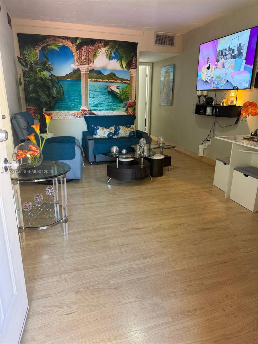 A living room features a tropical wall tapestry, blue seating, and a wall-mounted television — 1245 W 24th St # 118, Hialeah FL 33010, HIALEAH, FL