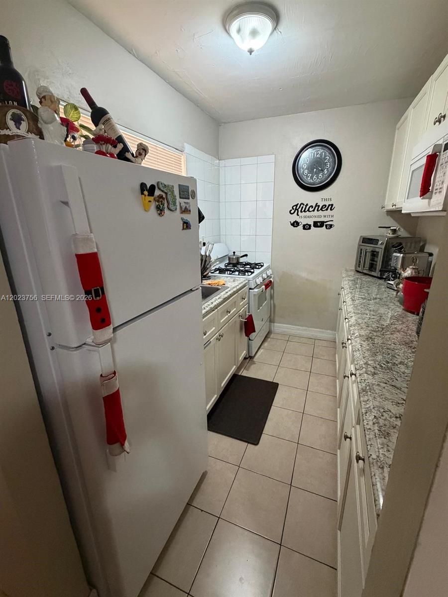 A narrow galley kitchen features white cabinets, granite countertops, tile flooring, and a white refrigerator — 1245 W 24th St # 118, Hialeah FL 33010, HIALEAH, FL