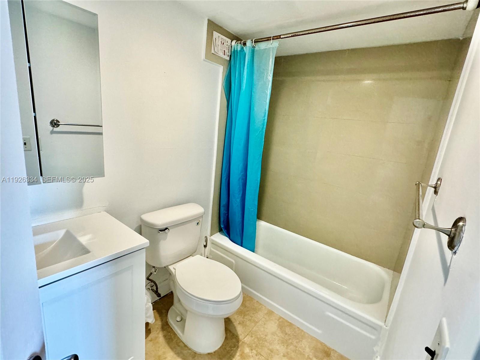 A bathroom features a white vanity, a toilet, and a bathtub with a blue curtain — 801 Three Islands Blvd # 417, Hallandale Beach FL 33009, HALLANDALE BEACH, FL
