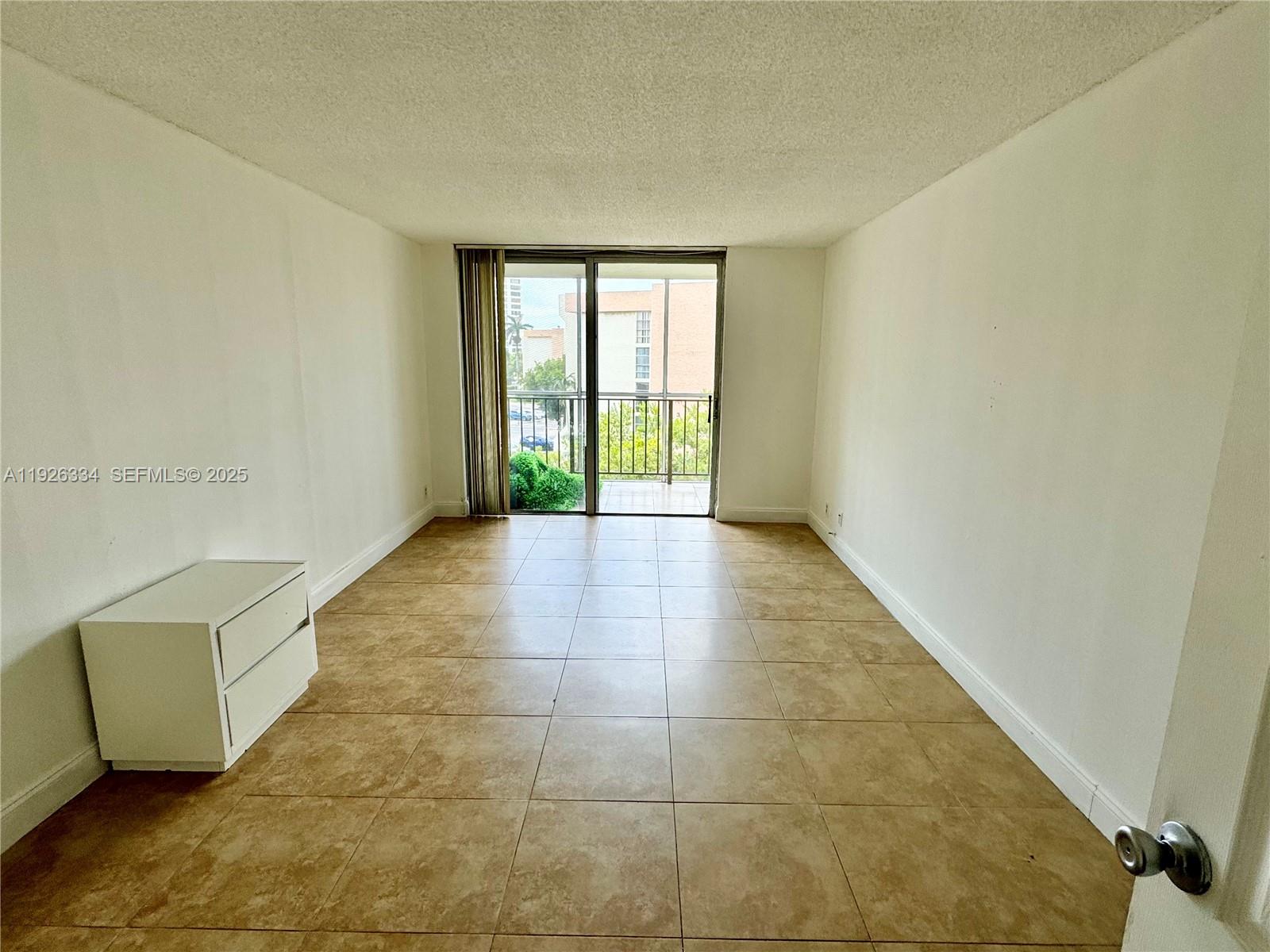 An empty room features beige tile flooring, white walls, and a sliding glass balcony door — 801 Three Islands Blvd # 417, Hallandale Beach FL 33009, HALLANDALE BEACH, FL