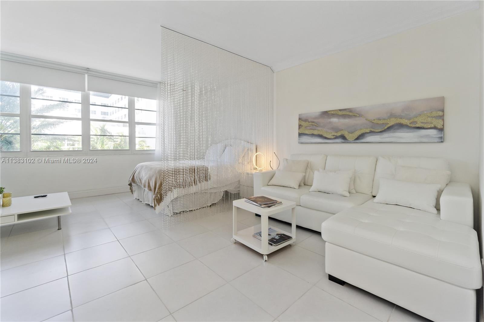 A studio apartment features white tile floors, a white sectional sofa, and a beaded room divider — 100 Lincoln Rd # 306, Miami Beach FL 33139, MIAMI BEACH, FL