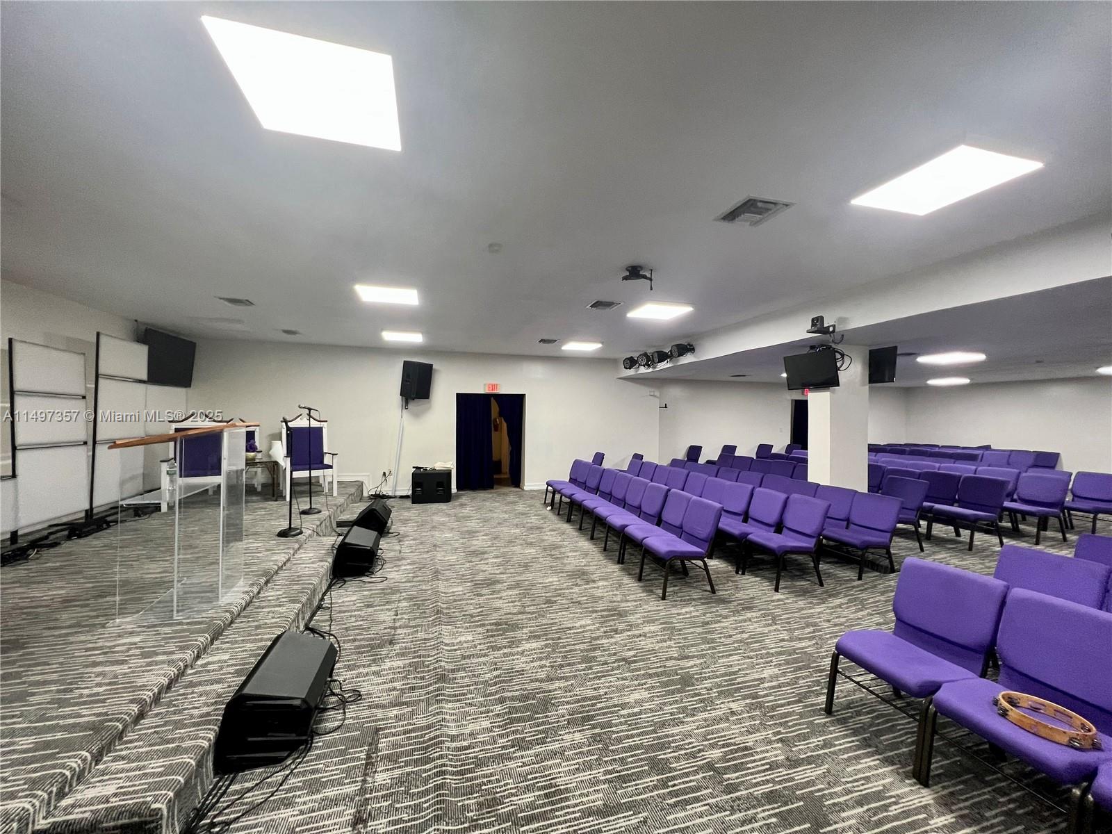 A church sanctuary features rows of purple chairs, a raised stage, and carpeted flooring — 6300 Pembroke Rd, Miramar FL 33023, MIRAMAR, FL