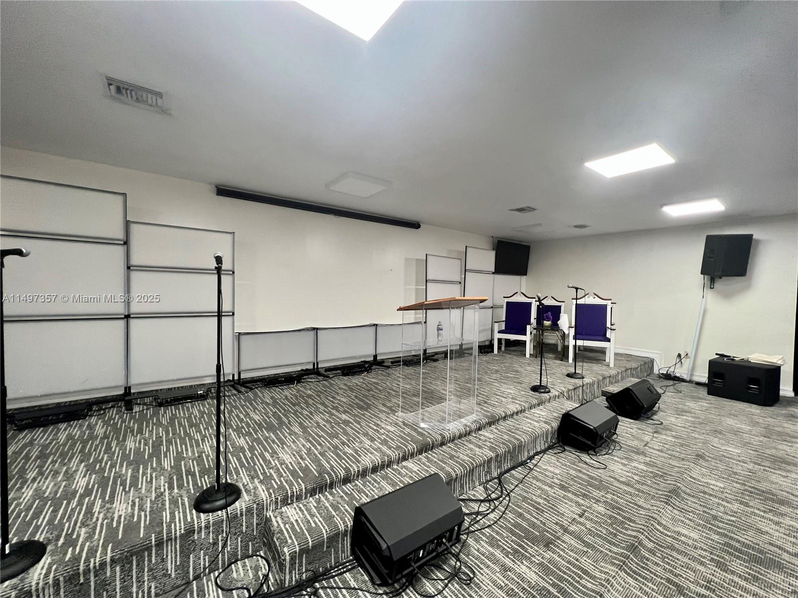 A raised stage features a clear podium, two purple chairs, and audio equipment — 6300 Pembroke Rd, Miramar FL 33023, MIRAMAR, FL