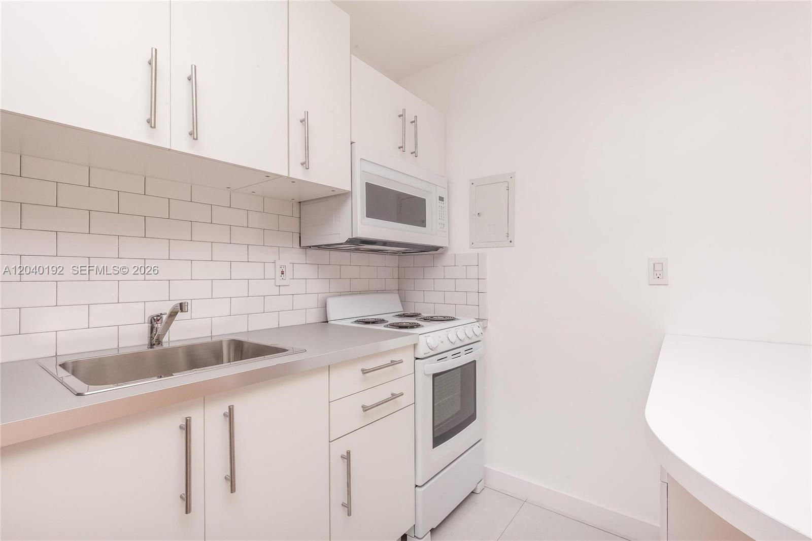 A white kitchen features subway tile backsplashes, stainless steel sink, and white cabinetry — 345 Michigan Ave # 20, Miami Beach FL 33139, MIAMI BEACH, FL