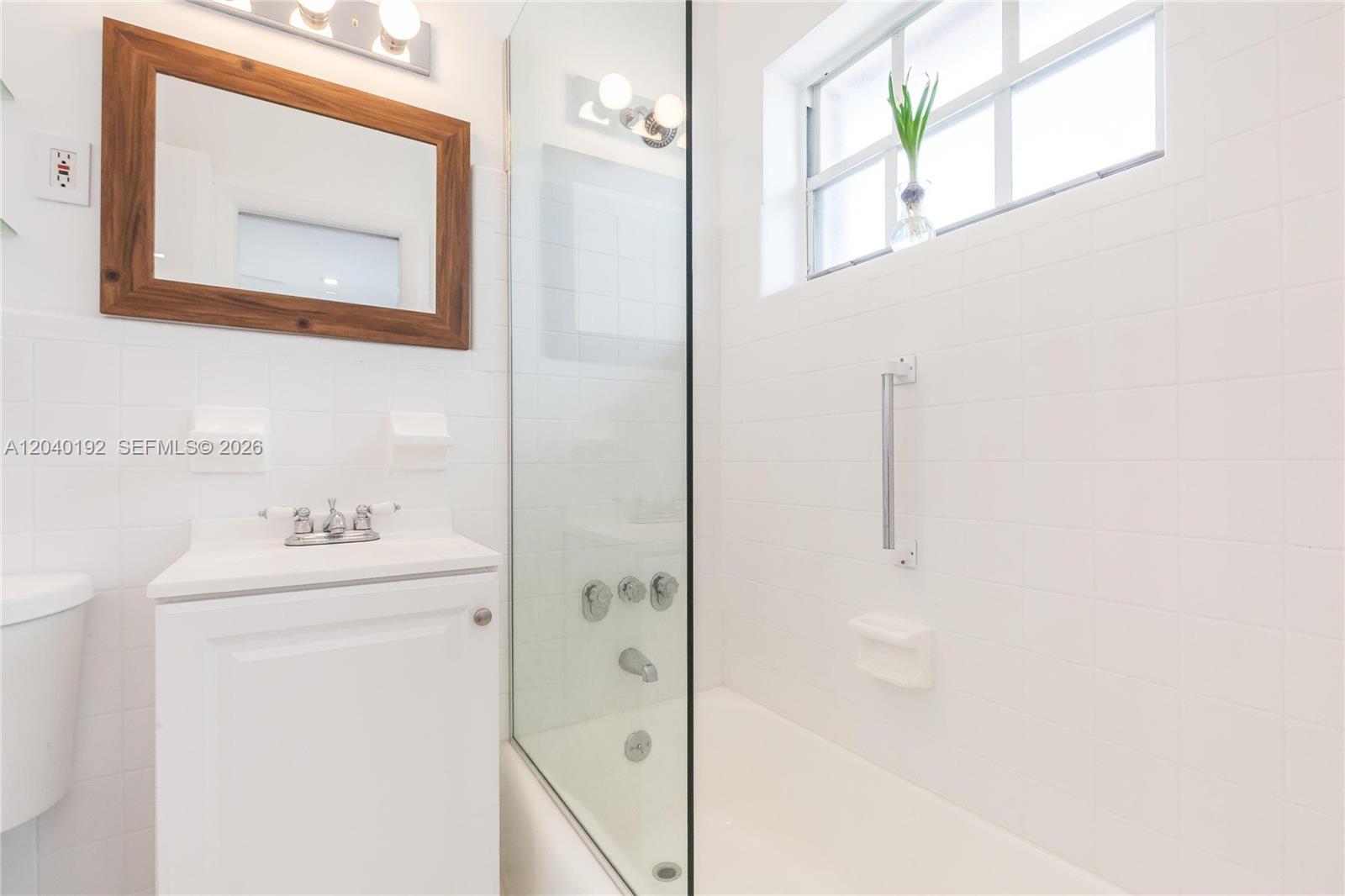 A bathroom features a white vanity, a wooden-framed mirror, and a tiled shower-tub combination — 345 Michigan Ave # 20, Miami Beach FL 33139, MIAMI BEACH, FL