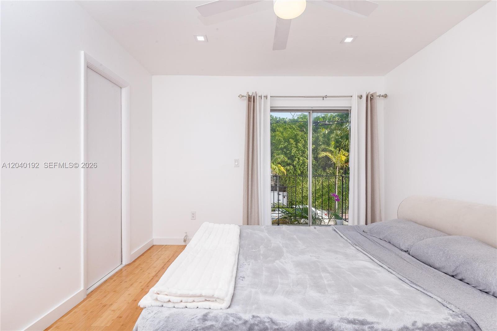 A bedroom features a bed, light wood flooring, white walls, and a sliding glass door — 345 Michigan Ave # 20, Miami Beach FL 33139, MIAMI BEACH, FL