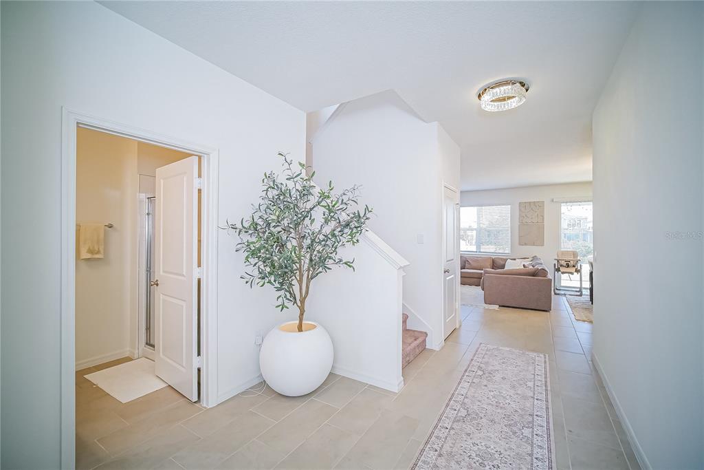 A bright entryway features tile flooring, a potted olive tree, and stairs leading to the second floor — 895 OVERPOOL AVENUE, DAVENPORT, FL