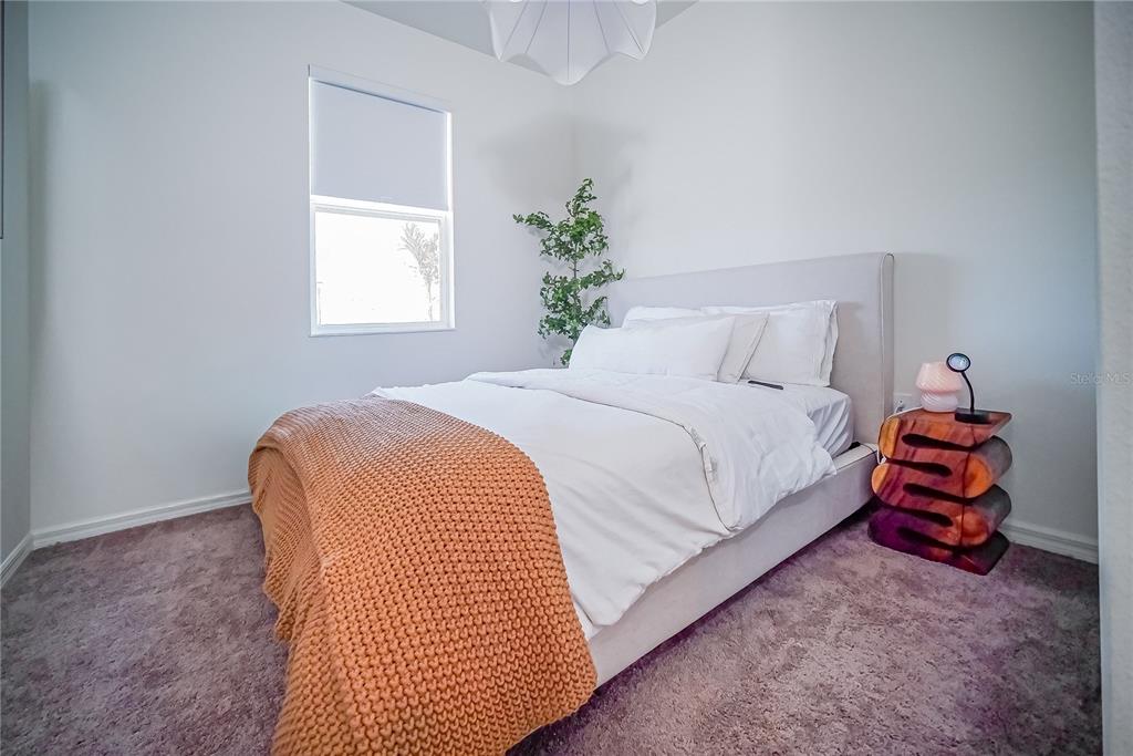 A bedroom features a bed with a chunky orange throw, a unique side table, and carpet — 895 OVERPOOL AVENUE, DAVENPORT, FL