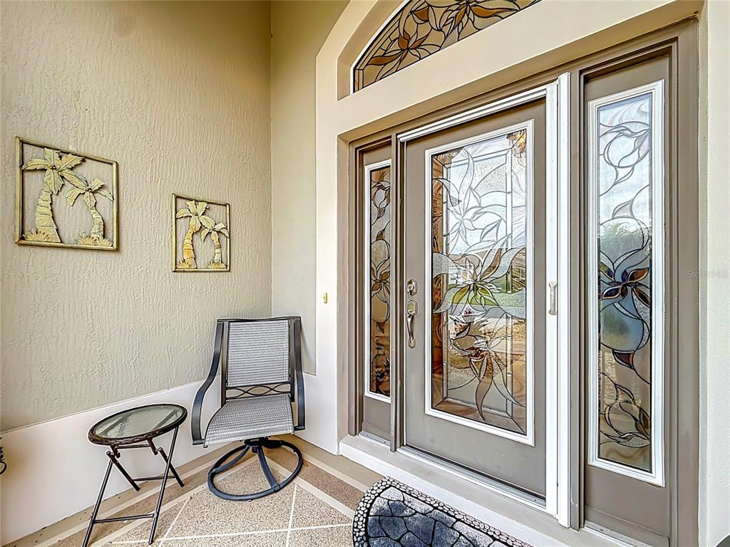 A covered entryway features a front door with stained glass panels and a small patio chair — 1967 FLOWERSVILLE PLACE, THE VILLAGES, FL