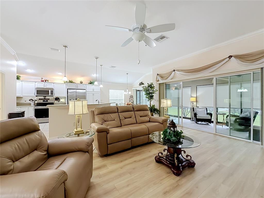 A living room with light wood floors, a tan sofa, and sliding doors to a patio — 1967 FLOWERSVILLE PLACE, THE VILLAGES, FL